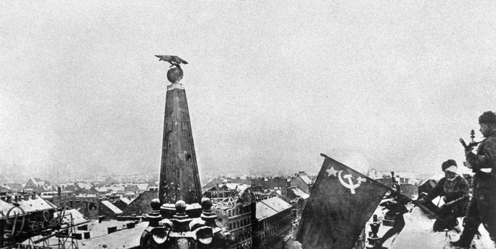 Старший сержант Евгений Костерев и младший сержант Александр Пертяков из 1405-го зенитного артиллерийского полка 38-й зенитно-артиллерийской Черкасской Краснознамённой дивизии Резерва Главного Командования устанавливают советский флаг над Будапештом. © РИА Новости / В. Милосердов